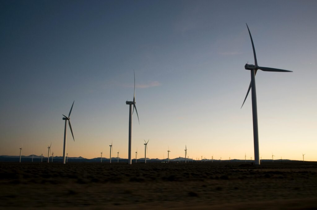 Row of white wind turbines on green field under blue sky, representing renewable energy for Scope 2 emissions accounting.
